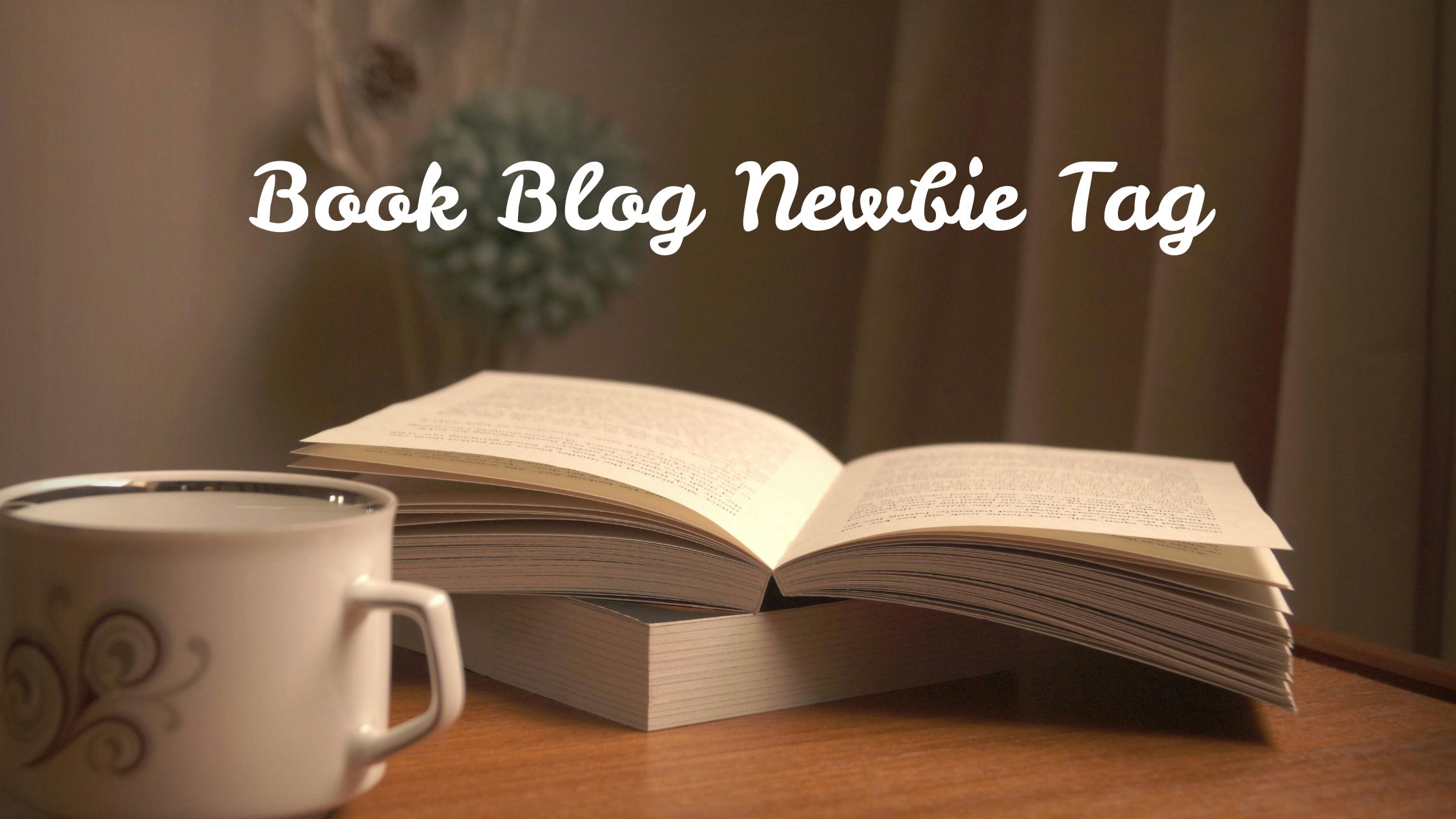 Features an open book stacked on a closed one on a table with a drink in a mug